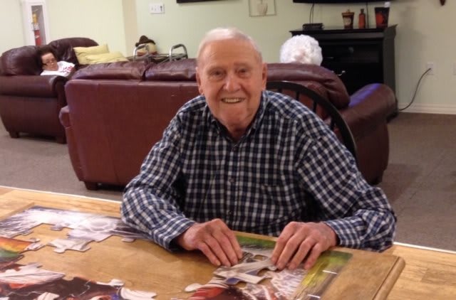 An elderly man smiling while sitting at a table indoors.