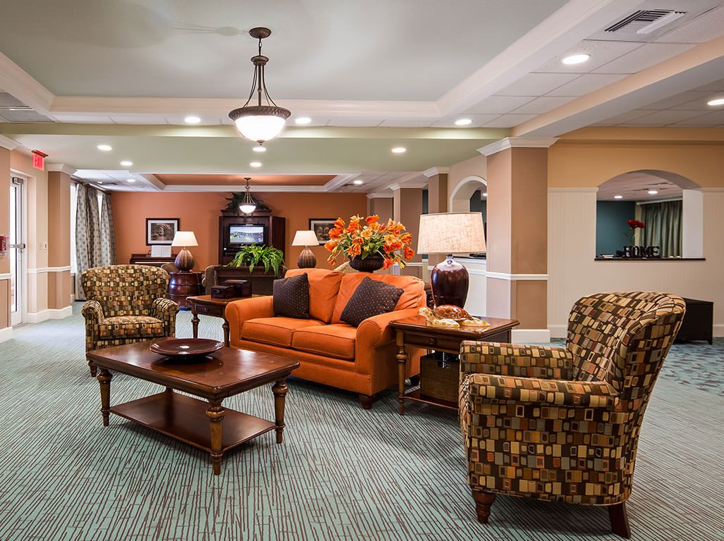 A cozy living room featuring an orange sofa, patterned armchairs, and a central coffee table under elegant lighting.