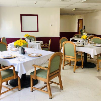 A neatly arranged dining area with tables set with white tablecloths and floral centerpieces.