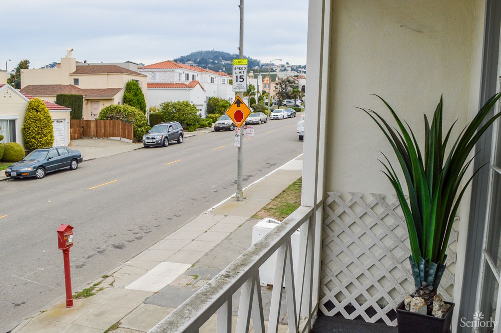 A view from a balcony overlooking a residential street with parked cars and houses.