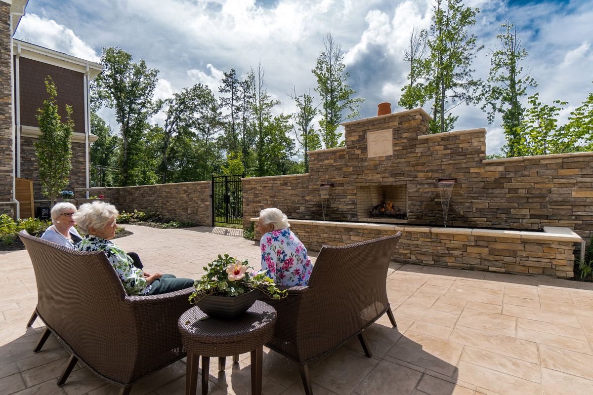 Two people sitting on a patio surrounded by nature, enjoying a peaceful outdoor setting with a large stone fireplace.
