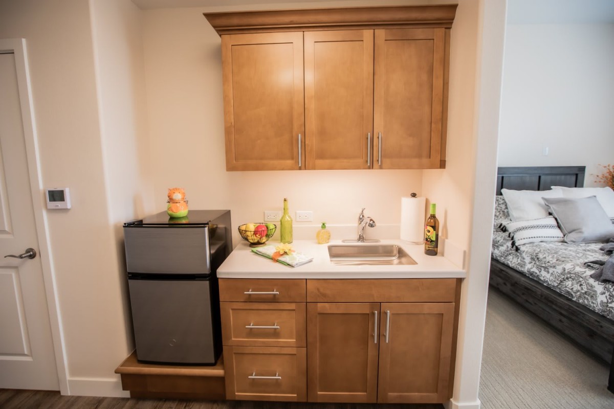 A small kitchenette with wooden cabinets, a mini fridge, and a countertop with a sink.
