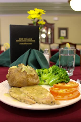 A delicious meal featuring chicken, broccoli, baked potato, and sliced tomatoes served in a restaurant setting.
