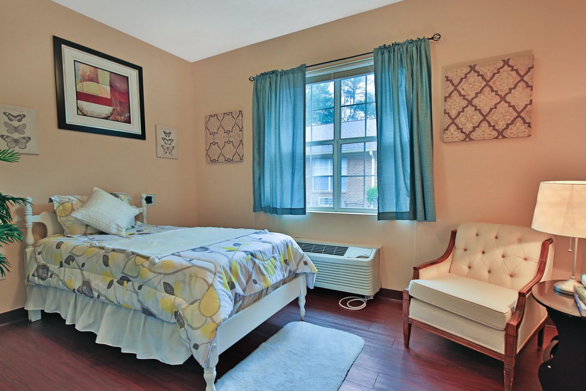 A cozy bedroom with a single bed, blue curtains, and an armchair by the window.