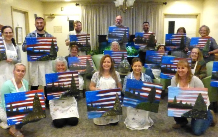 A group of people proudly displaying their completed landscape paintings in a class setting.