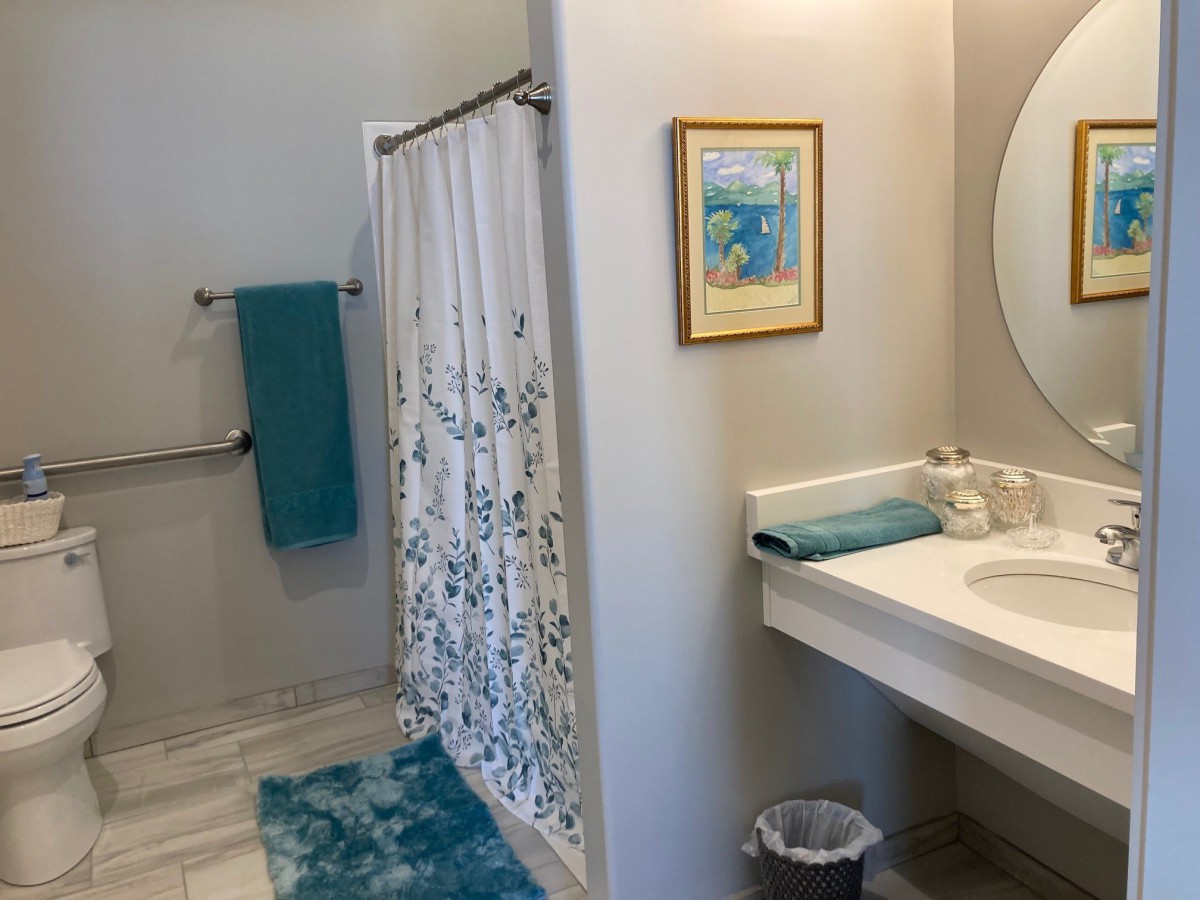 A clean and bright bathroom with turquoise accents, featuring a shower curtain, sink, mirror, and colorful towels.