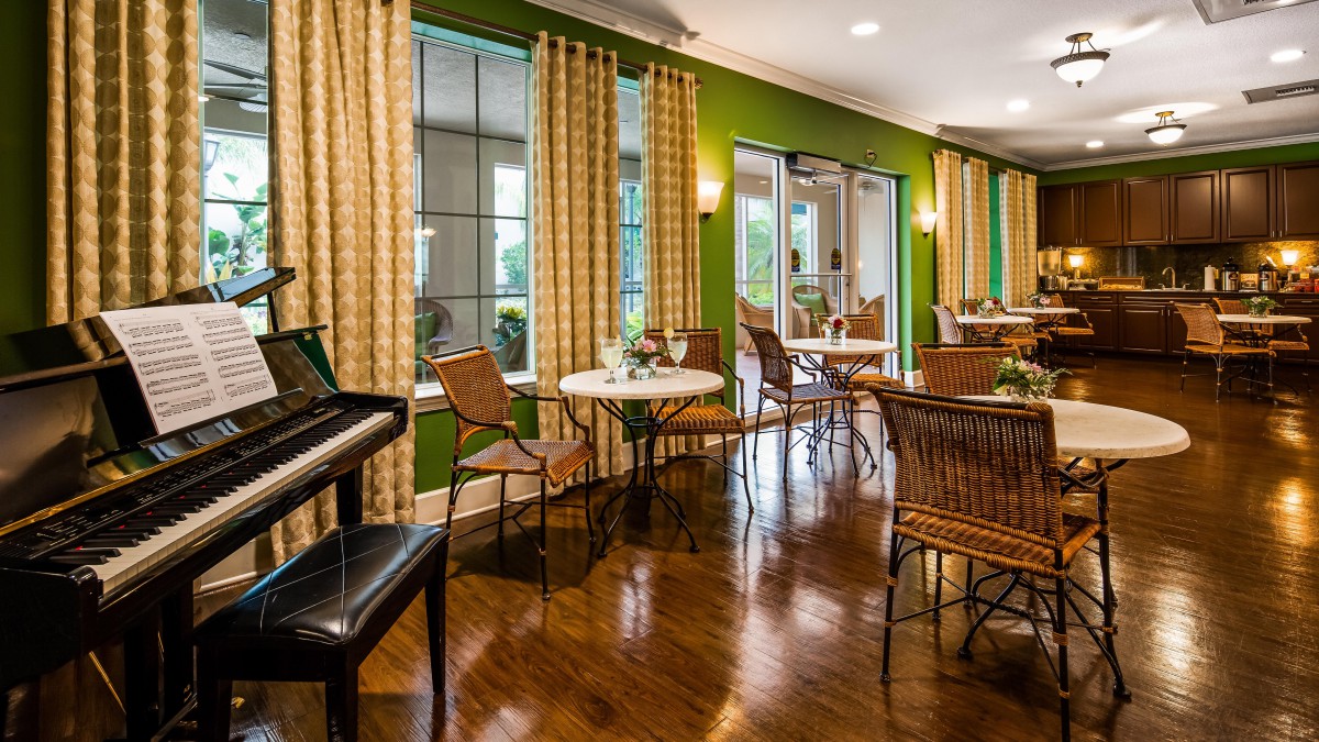 A cozy dining area with a piano, featuring wooden floors and large windows adorned with curtains.