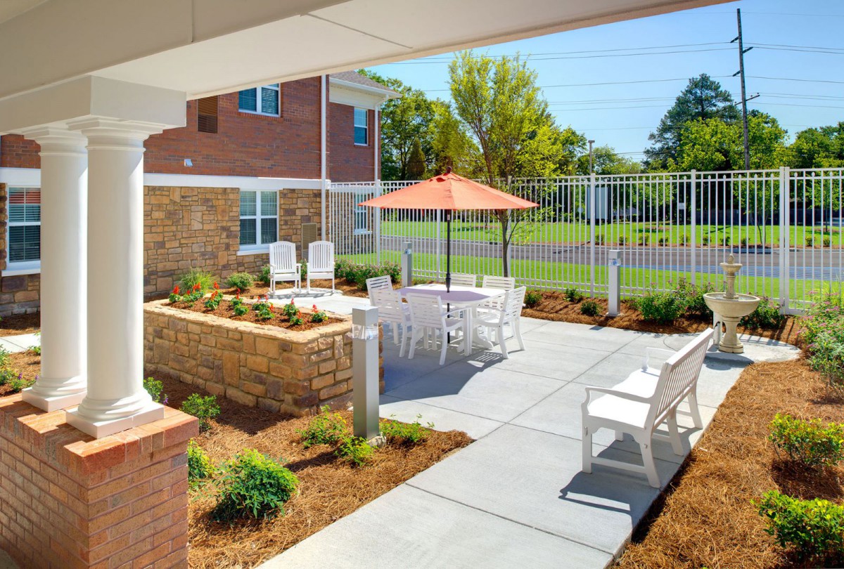An inviting outdoor patio area with seating and an umbrella, surrounded by landscaped gardens.