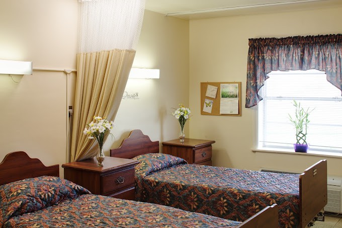 A cozy bedroom with two beds featuring floral bedspreads, nightstands, and a curtained window.