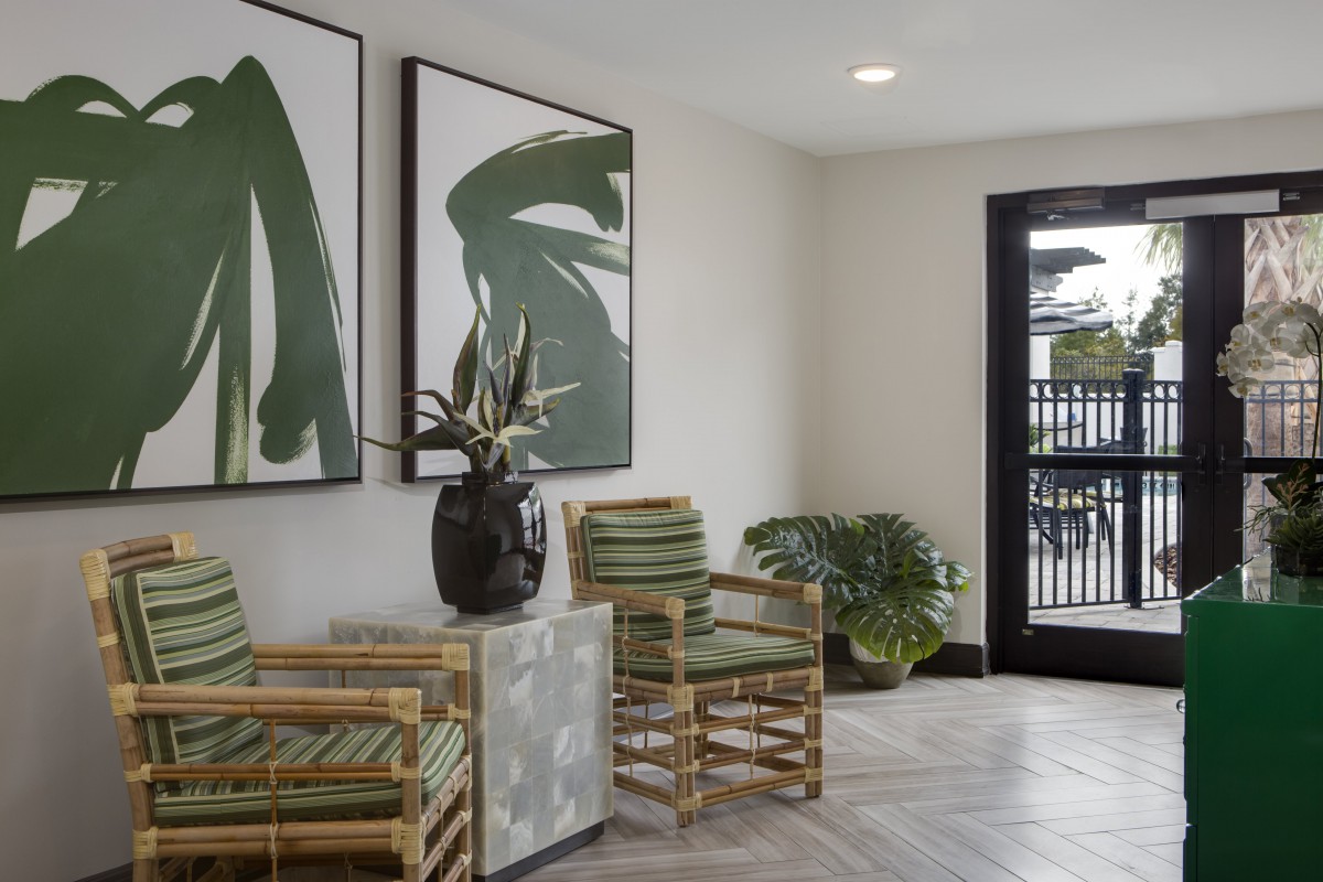 A modern lobby area featuring minimalist decor, including green striped chairs, large botanical artwork, and lush plants.