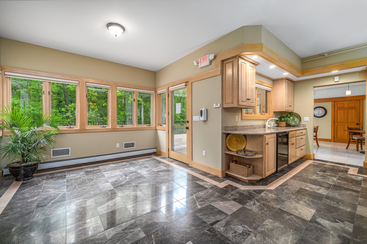 A modern kitchen with wood cabinets, large windows, and a sleek tile floor.