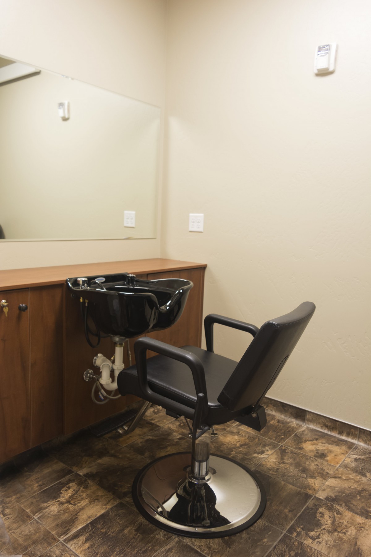 A salon hair washing station with a chair and mirror.