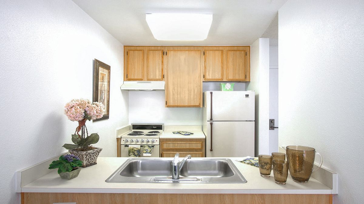 A compact kitchen with wooden cabinets, a stainless steel refrigerator, and a double sink.