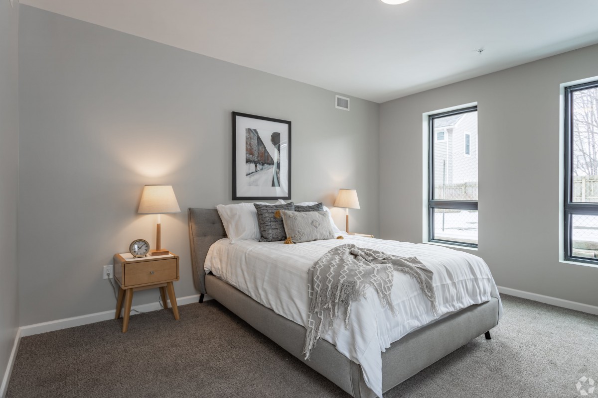 A modern bedroom featuring a neatly made bed with decorative pillows, two bedside tables with lamps, and a minimalist wall art piece.