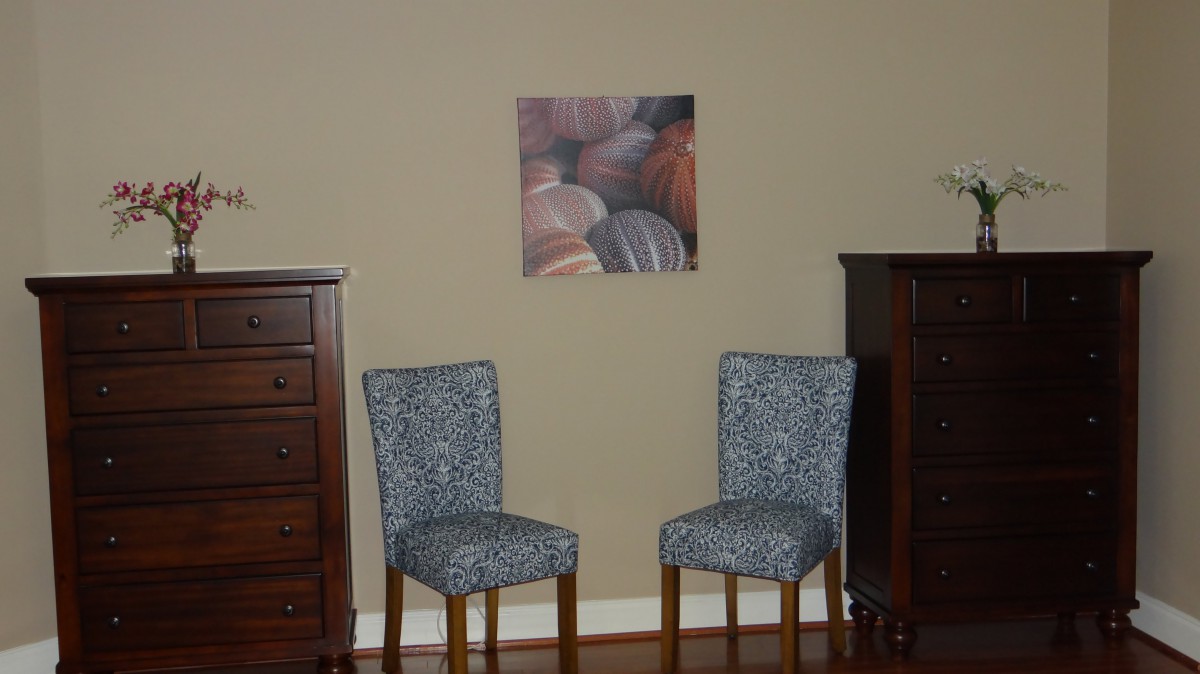 A room interior featuring two patterned chairs, a dresser on each side, and a piece of wall art.