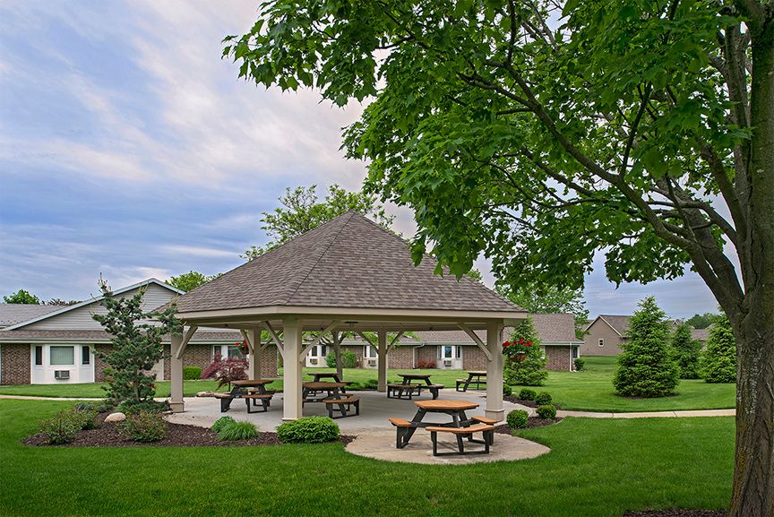 A serene park featuring a gazebo surrounded by lush greenery and picnic tables.