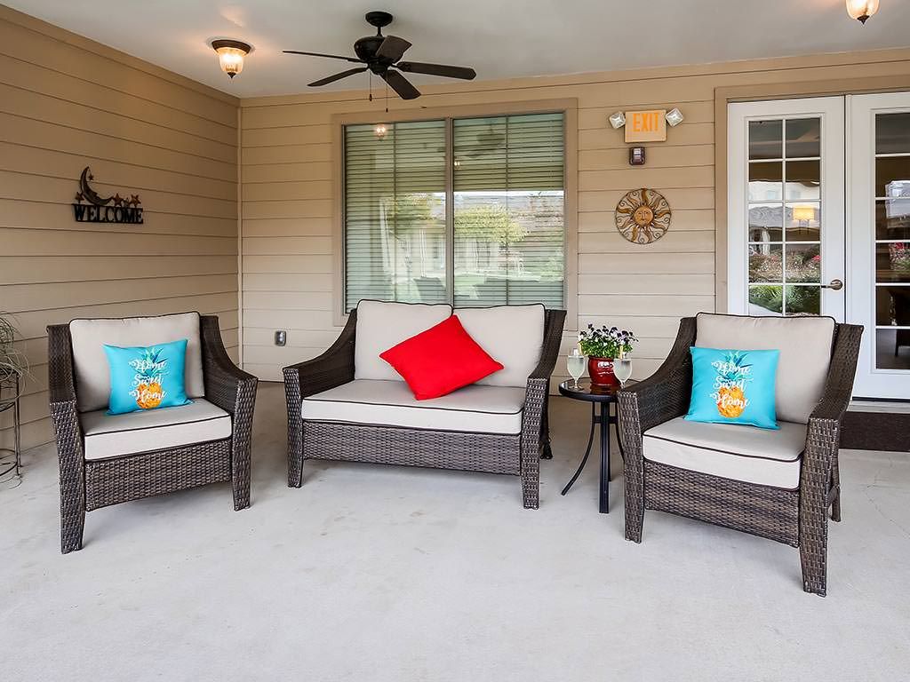 An inviting outdoor patio area featuring comfortable wicker furniture with colorful cushions, a ceiling fan for comfort, and decorative elements adding charm to the space.