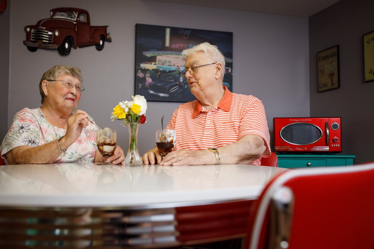 Elderly couple enjoying drinks and conversation in a retro-themed diner.