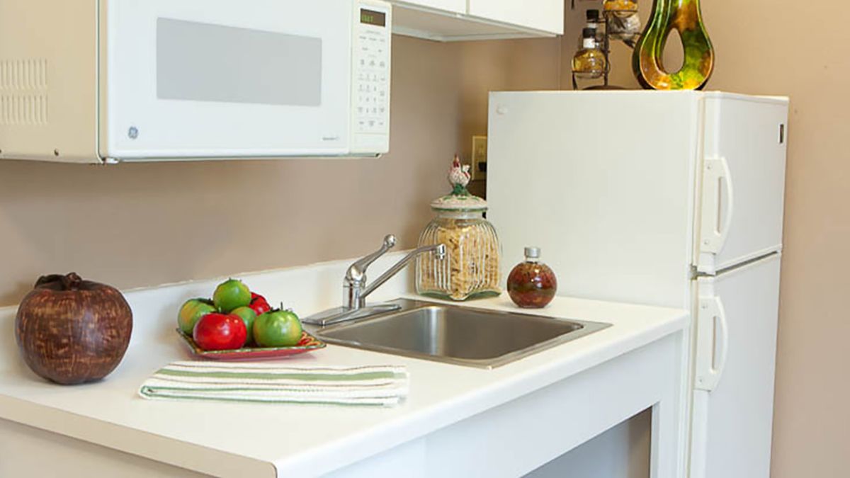 A clean kitchen counter with a sink, microwave, and apples on the countertop.