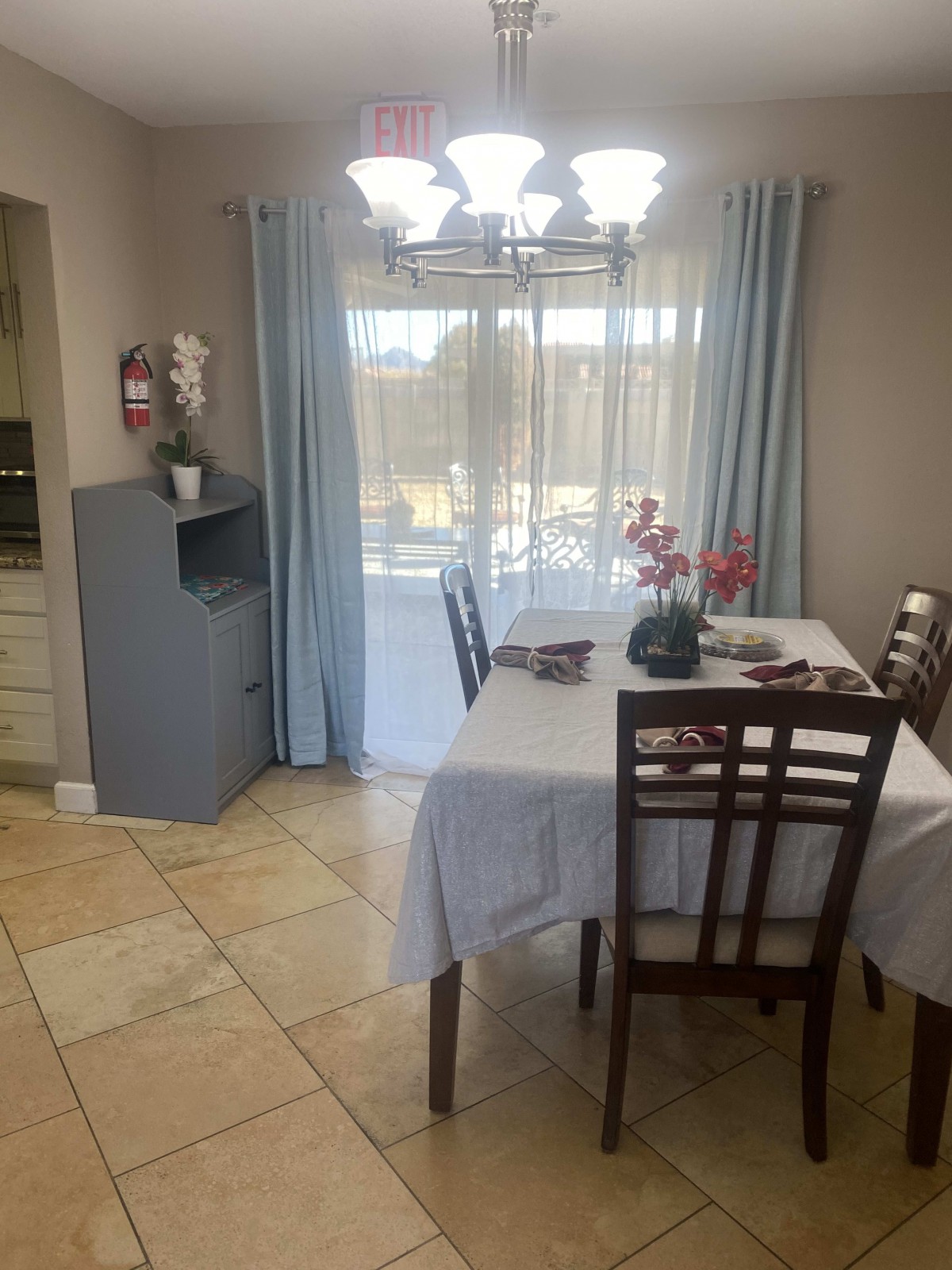 A cozy dining area with a table set for four, decorated with flowers near a window with light blue curtains.