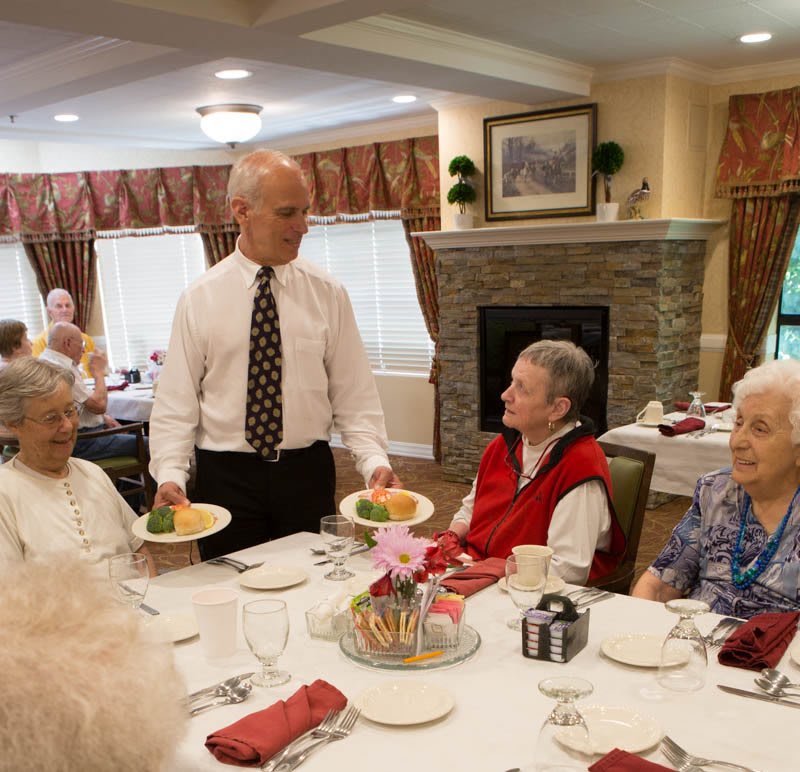 A server delivers meals to a group of elderly individuals dining together.