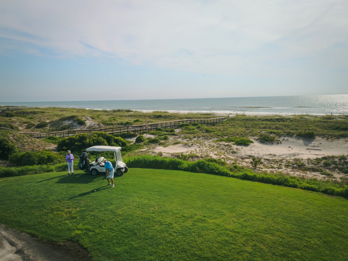 A scenic view of a golf course by the ocean with a golf cart and players preparing for their game.