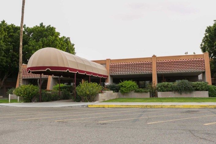 A restaurant exterior with a large awning and an empty parking lot in a desert setting.