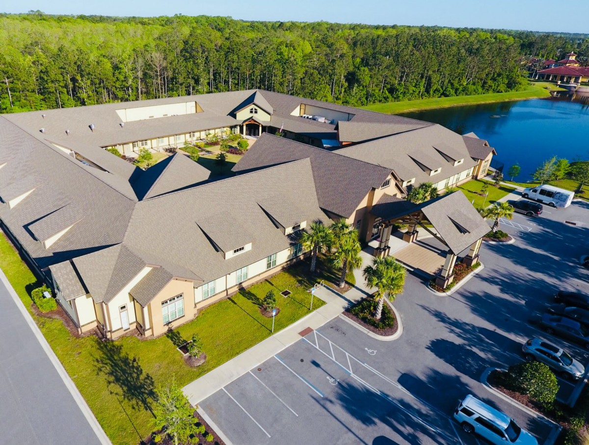 Aerial view of a large building complex surrounded by a parking lot, with a lake and lush greenery nearby.