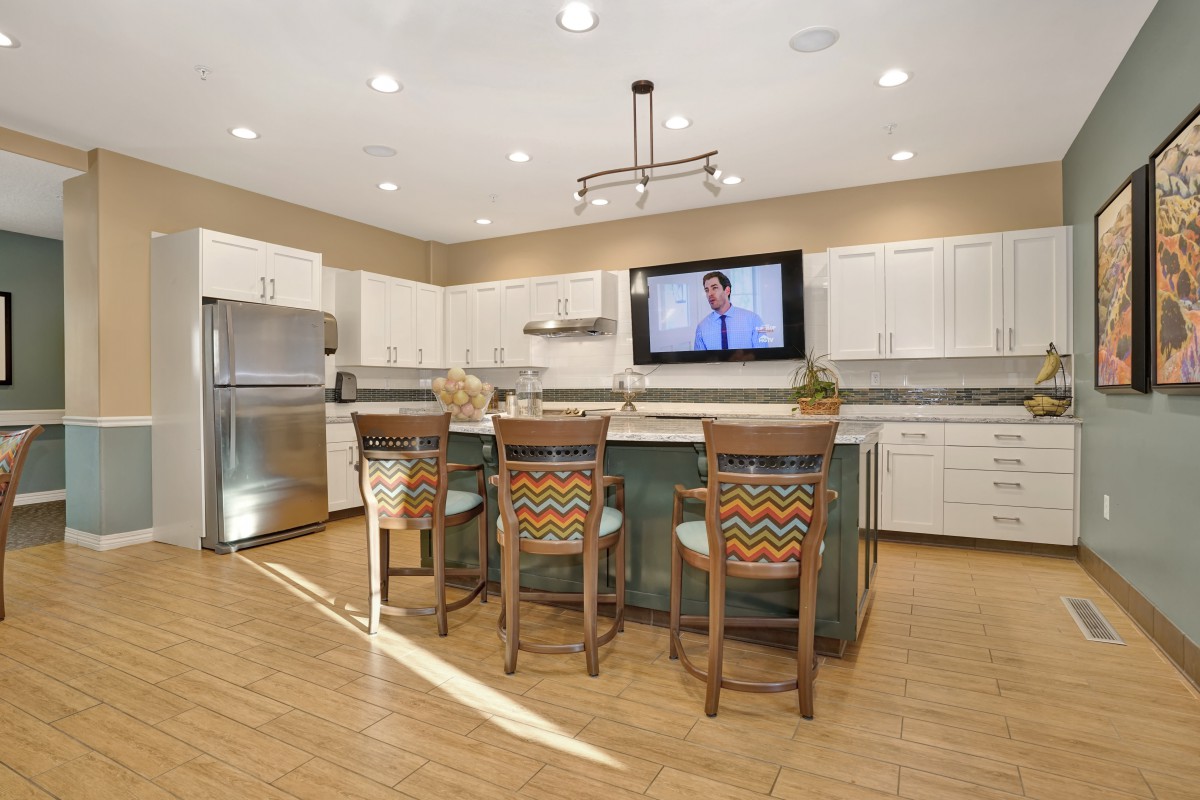 A modern kitchen with an island, bar stools, and a television mounted on the wall.