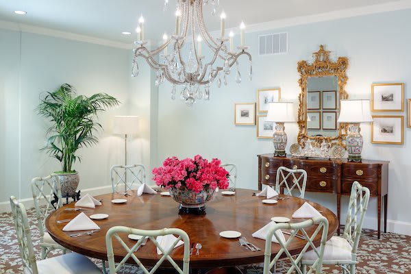 An elegant dining room with a chandelier and a round table featuring a floral centerpiece.
