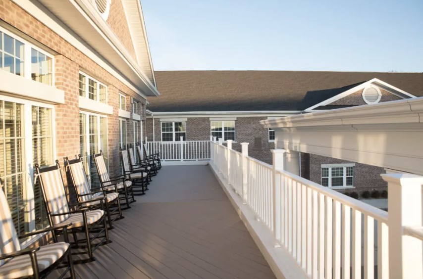 A spacious balcony with a row of rocking chairs and white railings, attached to a building.