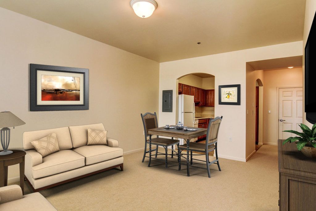 A modern living room with a dining area, featuring a sofa, dining table with chairs, and artwork on the walls. The kitchen can be seen in the background.