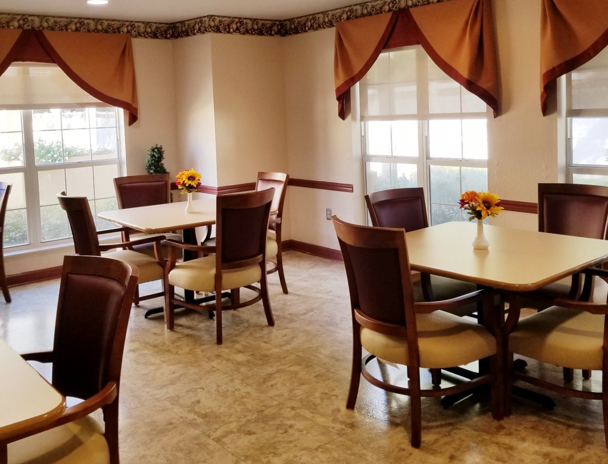 A cozy dining area with tables and chairs, decorated with flowers and curtains.