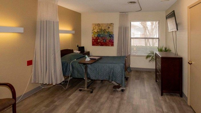A clean and modern hospital room with a bed and medical equipment, decorated with colorful artwork on the wall.