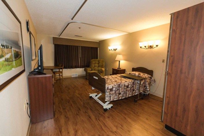 A well-lit hospital room with a single bed and wooden flooring.