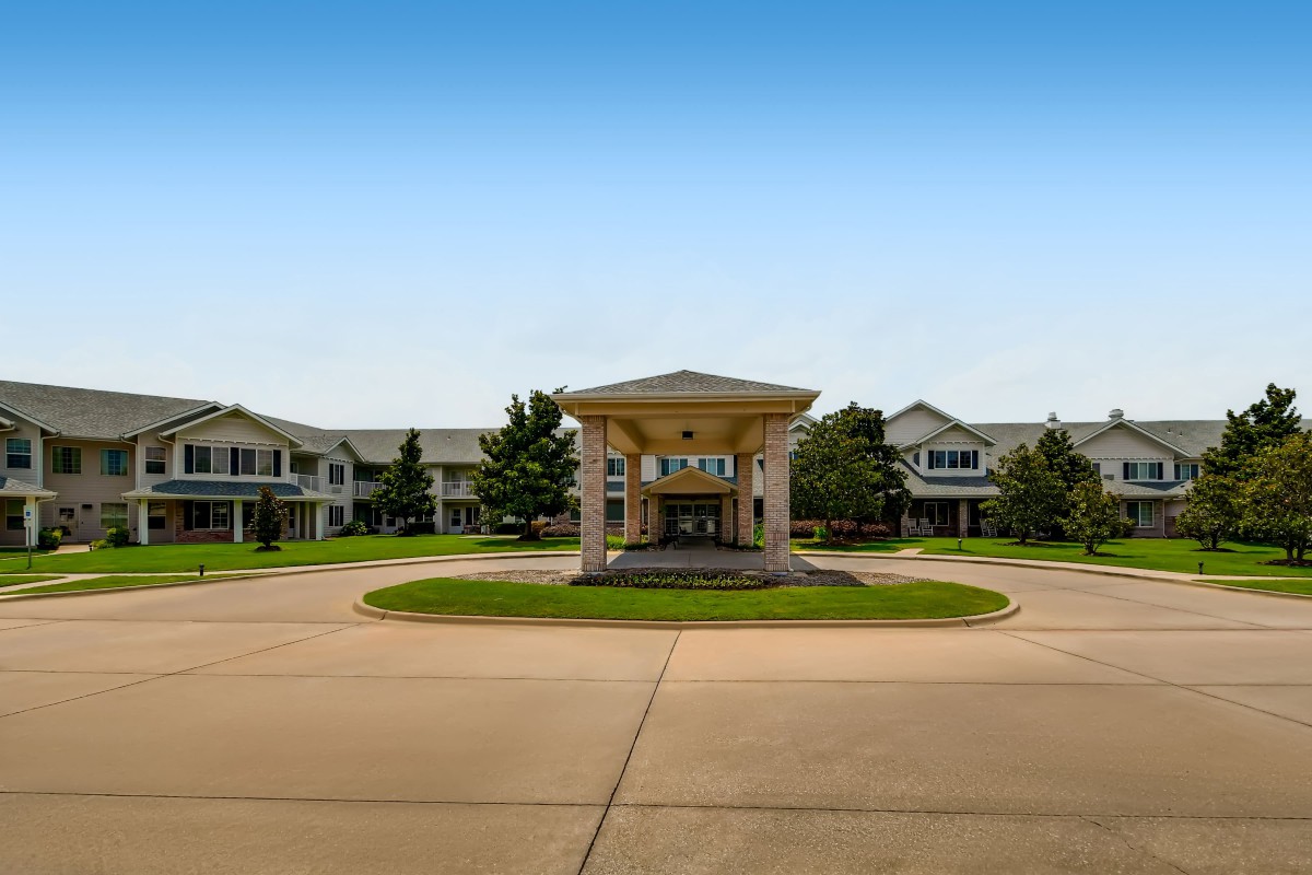 A wide driveway leading to the entrance of a large residential building, surrounded by well-maintained landscaping.
