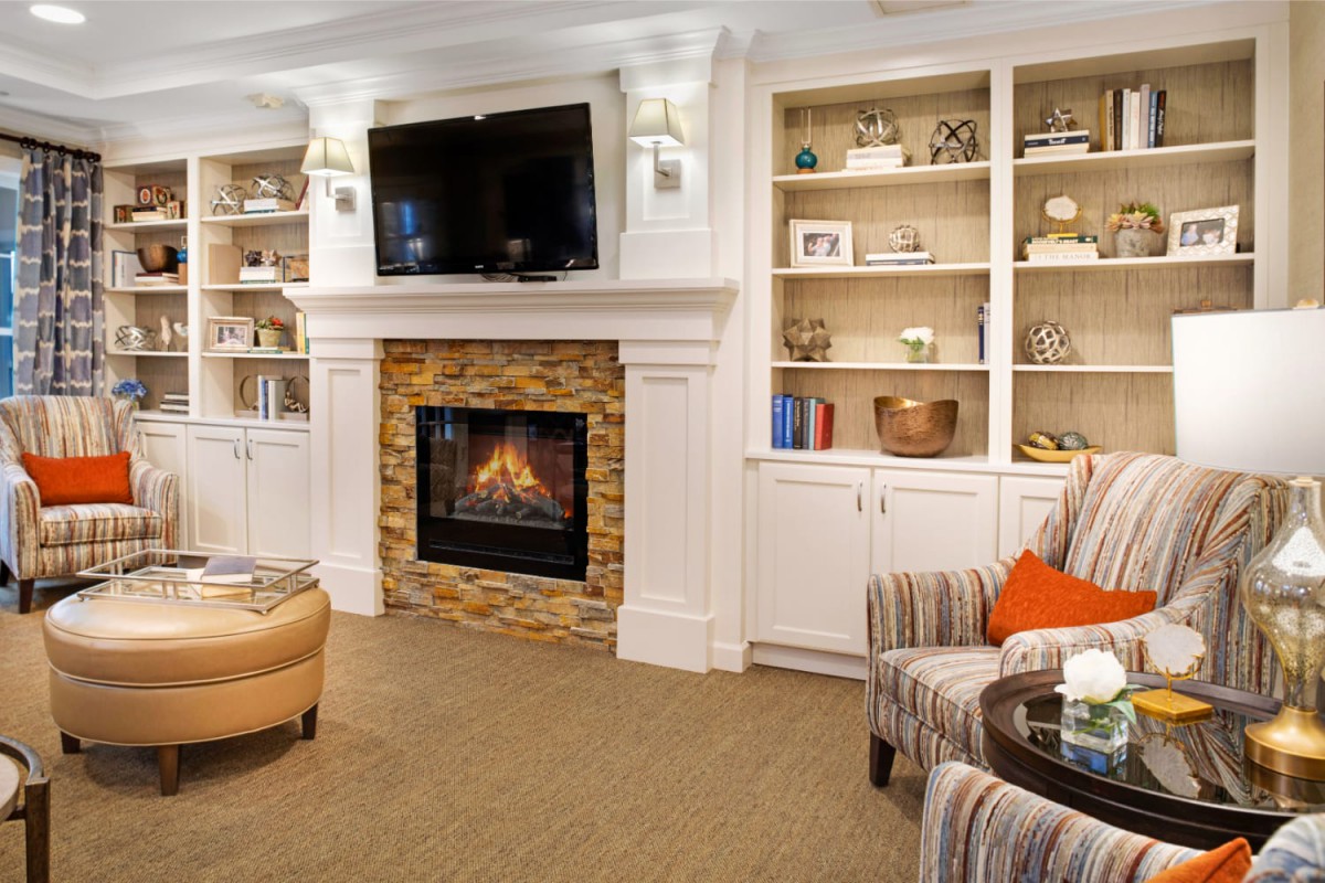 A cozy living room with a fireplace and built-in bookshelves, featuring a comfortable armchair and a wall-mounted television.