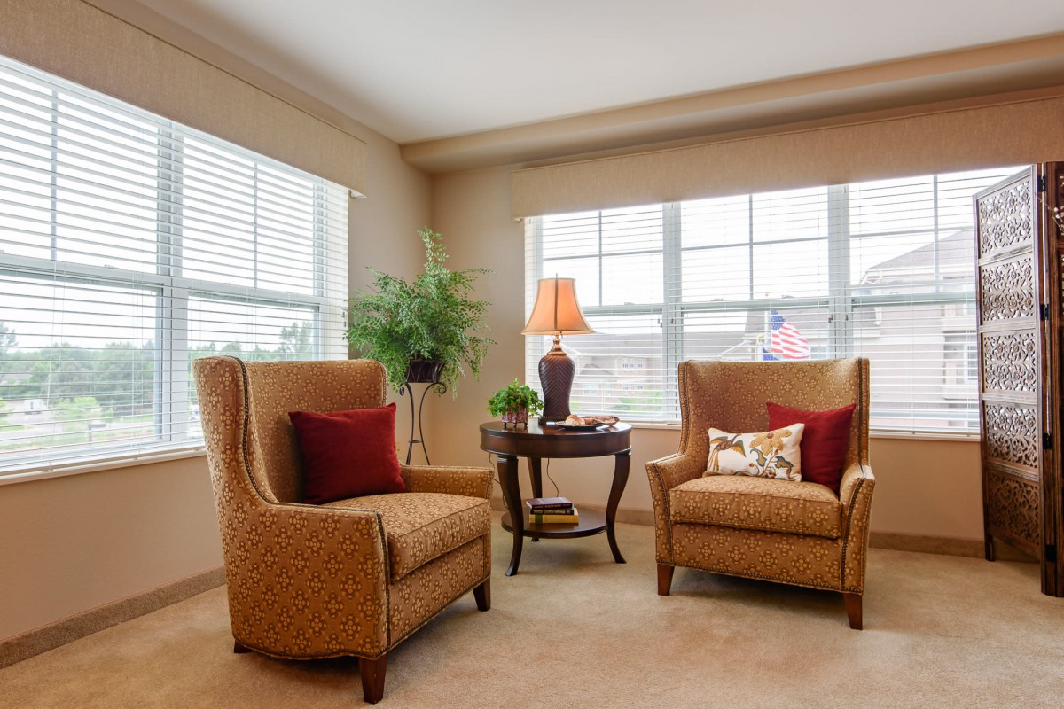 A cozy living room corner with two armchairs, a small table, and a lamp by the window.
