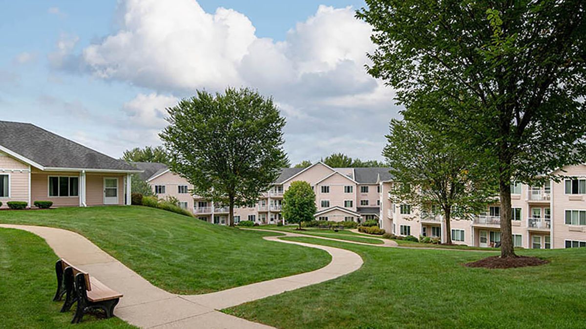A scenic view of residential apartment buildings surrounded by lush green lawns and trees under a partly cloudy sky.
