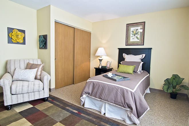 A cozy bedroom featuring a single bed, side table with a lamp, and minimalist decor.