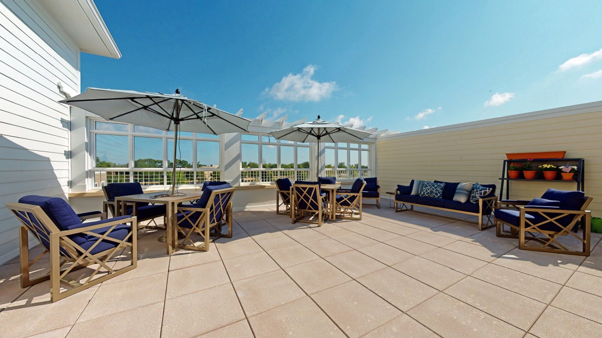 A spacious rooftop terrace with outdoor seating and umbrellas under a clear blue sky.
