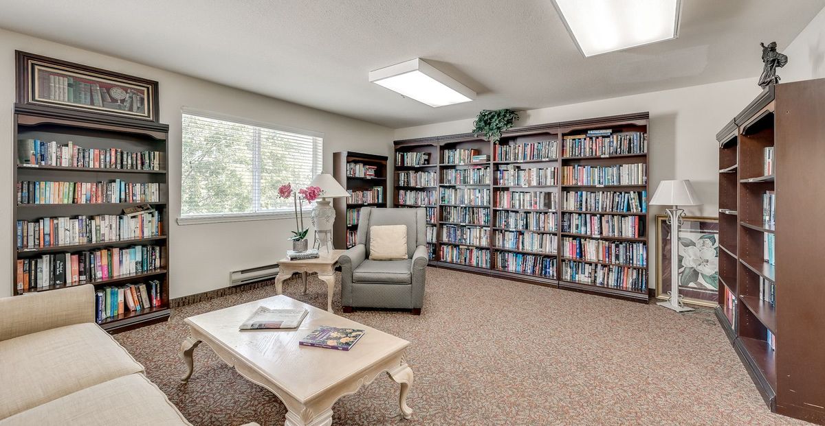 A cozy library reading room with bookshelves, an armchair, and a table near a window.
