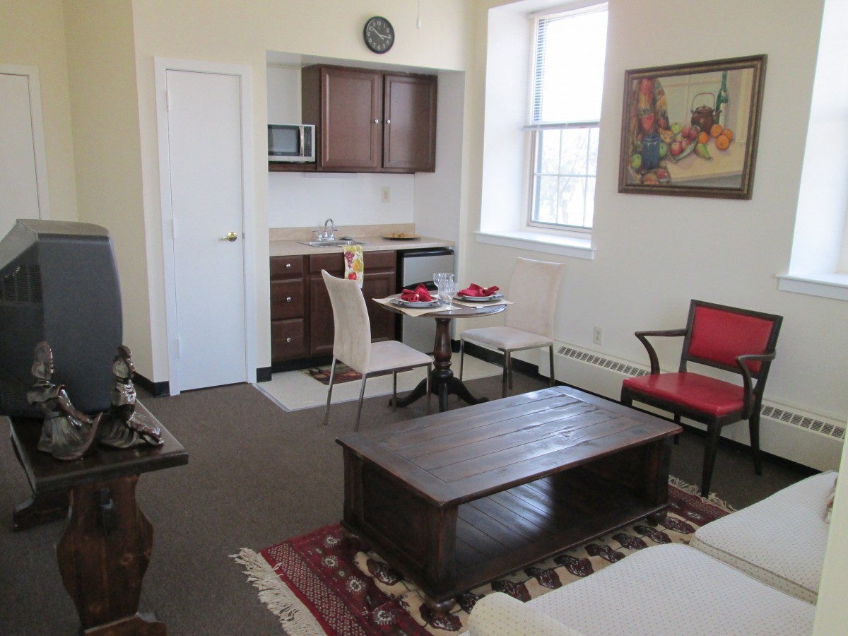 A cozy studio apartment featuring a small kitchen area, dining table with chairs, and comfortable seating.