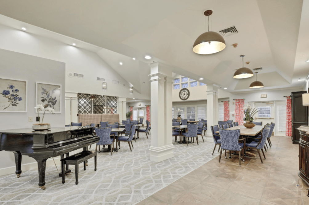 A spacious dining area with tables and chairs, featuring a piano and decorative lighting.