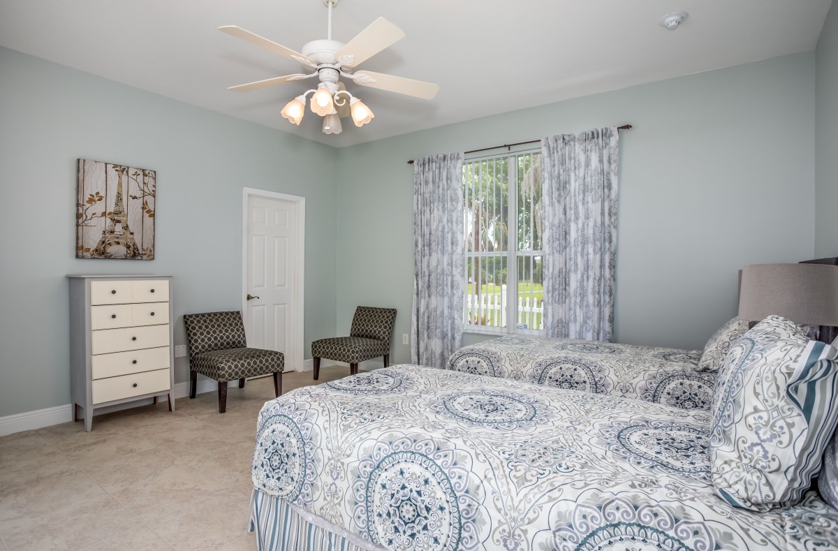 A cozy bedroom featuring twin beds with patterned bedding, a ceiling fan, and natural light coming through a window with curtains.