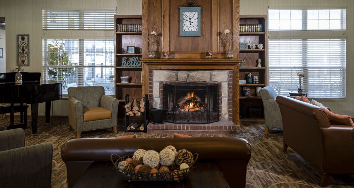 A cozy living room with a fireplace, surrounded by bookshelves and armchairs.