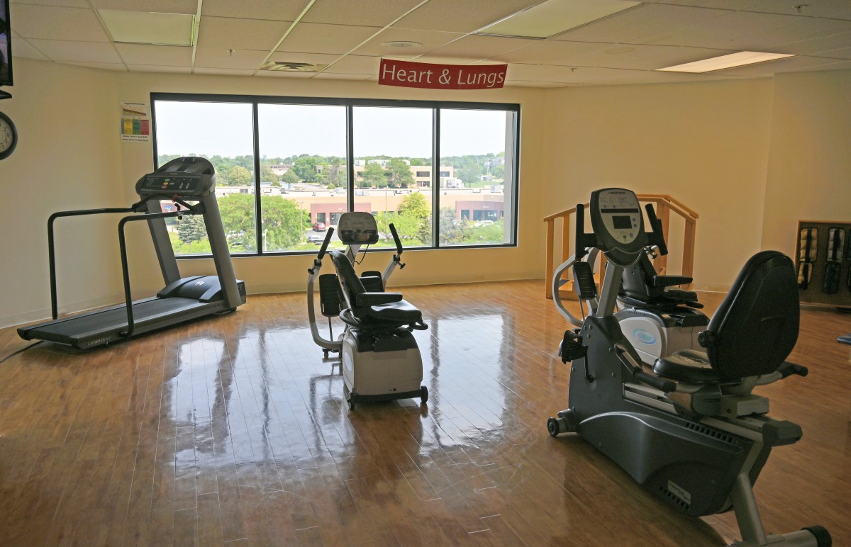 A bright gym room with exercise equipment including a treadmill and stationary bikes.