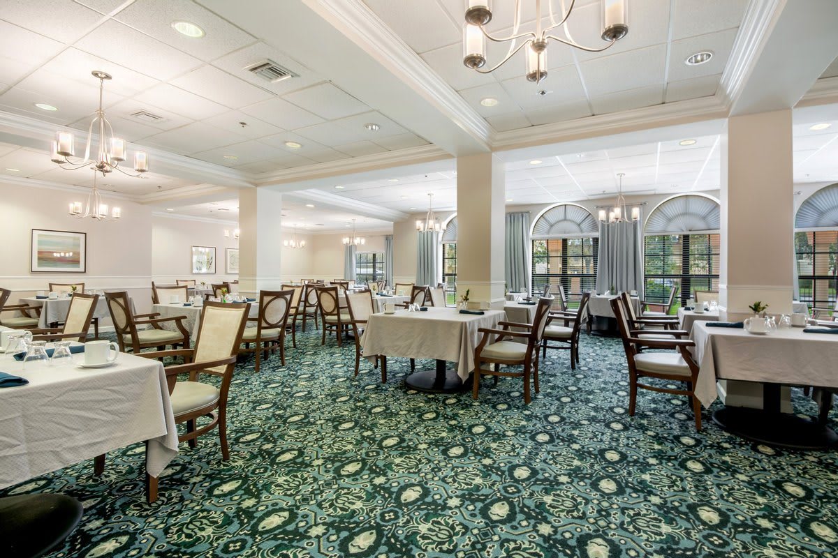 An elegant dining room featuring neatly arranged tables and chairs, with decorative chandeliers and a patterned carpet.