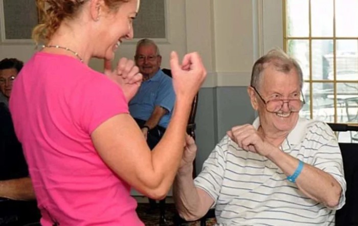 A caregiver engaging in a light exercise with an elderly person, promoting interaction and happiness in a nursing home setting.