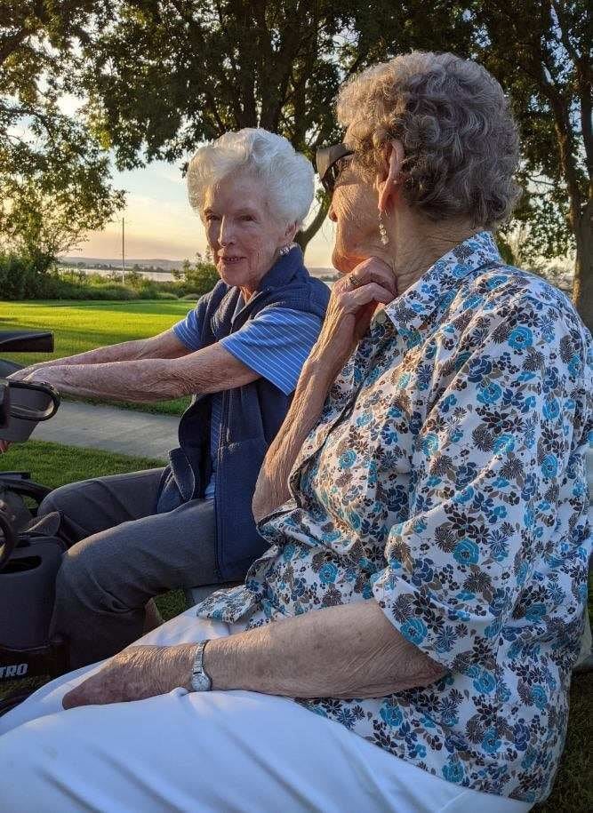 Two elderly women enjoying a conversation in the park during sunset.